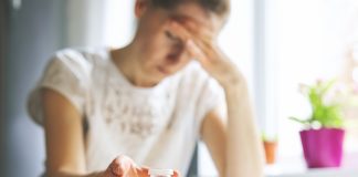 Antidépresseurs : Types, Usages et Effets Secondaires Personne fatiguée se tenant la tête avec un flacon de médicaments antidépresseurs devant elle