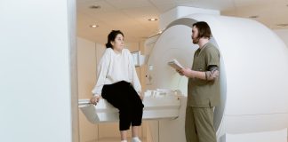 Claustrophobie : Qu’est-ce que c’est, Symptômes, Causes et Traitement Technicien médical assistant une patiente avant un examen IRM, montrant la préparation pour les personnes souffrant de claustrophobie. La patiente en tenue décontractée est debout sur un marchepied près de la machine IRM, en discussion avec un professionnel de santé en uniforme vert.