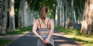 Tout Ce Qu’il Faut Savoir Sur le Type de Corps Ectomorphe Femme athlétique de type ectomorphe vue de dos, portant une tenue Gymshark, s'étirant dans une allée bordée d'arbres - illustration du mode de vie actif des personnes au corps ectomorphe