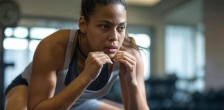 Exercice Anaérobie : Définition, Types et Bienfaits Une athlète féminine en plein exercice anaérobie, vêtue d'un débardeur gris et noir, est photographiée en plein effort dans une salle de sport. Elle est dans une position de préparation au sprint, concentrée, avec une expression intense sur son visage.