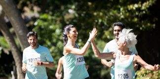 Entraînement au Semi-Marathon : Débutant 1 Coureurs heureux se tapant dans les mains pendant une course de semi-marathon, portant des dossards et des t-shirts turquoise dans un parc ensoleillé