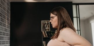 Les Raisons Surprenantes de Votre Prise de Poids Jeune femme ayant des problèmes de poids pinçant son ventre, portant des lunettes et un haut beige, illustrant les difficultés liées à la prise de poids inexpliquée et les préoccupations de santé - image liée aux causes médicales de la prise de poids