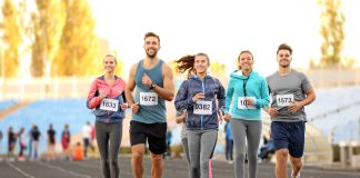 Entraînement au Semi-Marathon : Débutant 2 Groupe de coureurs souriants participant à un semi-marathon sur une piste d'athlétisme, portant des dossards numérotés et des tenues de course colorées