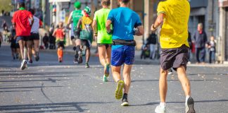 Entraînement au Semi-Marathon : Intermédiaire 1 Coureurs de semi-marathon vêtus de maillots colorés, vus de dos, participant à une course urbaine par une journée ensoleillée