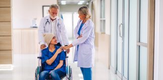 Soins Palliatifs : Objectif et À Quoi S’attendre Un médecin expérimenté et une infirmière offrant du soutien et du réconfort à une jeune patiente en fauteuil roulant dans un couloir d'hôpital, illustrant l'approche bienveillante et collaborative des soins palliatifs