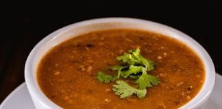 Meilleure Recette de Soupe de Lentilles Soupe de lentilles épicée végane servie dans un bol blanc, garnie de feuilles de coriandre fraîche. La texture crémeuse et la couleur ambrée de la soupe montrent une préparation parfaitement mijotée avec des épices.