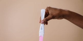 Grossesse – signes et symptômes Une main tenant un test de grossesse positif avec deux lignes visibles sur fond beige, symbolisant la détection précoce de la grossesse.