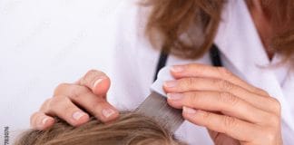 Poux de Tête : Signes, Symptômes, Causes et Traitement Un professionnel de santé en blouse blanche peignant délicatement les cheveux d’un enfant avec un peigne à lentes pour détecter les poux de tête, dans un cadre médical propre et lumineux, avec un microscope en arrière-plan, illustrant un examen médical pour les poux.