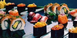 Combien de calories dans vos sushi préférés ? Assortiment varié de sushi frais incluant des rolls au saumon, nigiri au thon, maki, gunkan aux œufs de saumon et rolls californiens, présentés élégamment sur une assiette moderne avec des garnitures colorées et herbes fraîches