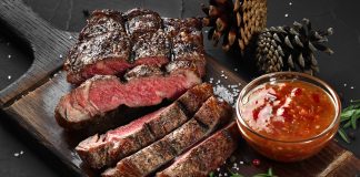 Arrêter la viande : 10 effets sur votre corps et votre santé Steak de bœuf grillé saignant tranché sur planche en bois avec sauce, romarin et sel, exemple de viande rouge associée à l'inflammation et au cholestérol élevé.