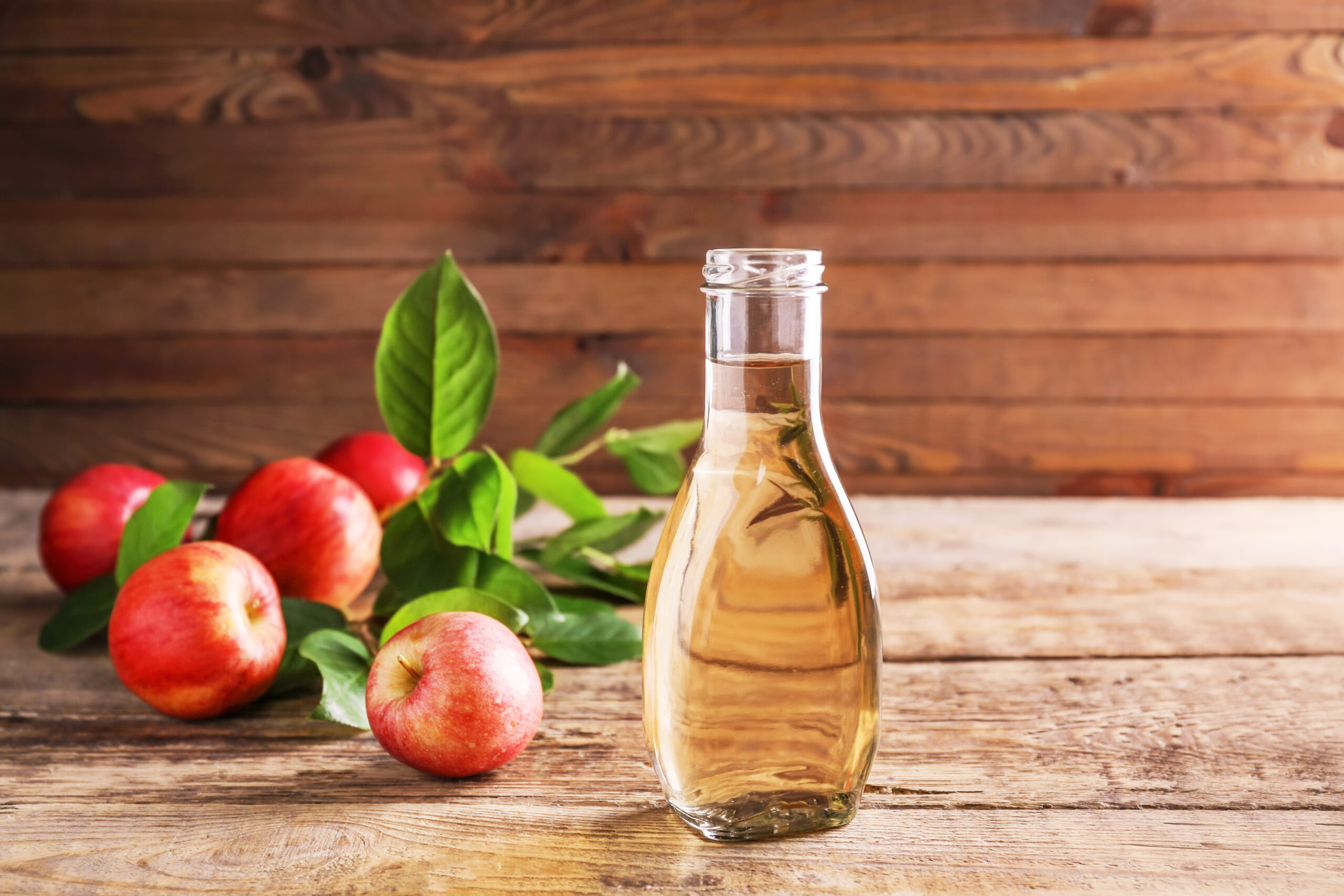 6 Bienfaits du Vinaigre de Cidre pour la Santé Bouteille de vinaigre de cidre entourée de pommes rouges et de feuilles vertes sur une table en bois, illustrant les bienfaits naturels du vinaigre de cidre pour la santé.