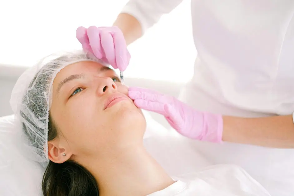 Professionnel de santé injectant du Botox sur le visage d’une patiente dans un cadre clinique, avec des gants roses et un environnement stérile.