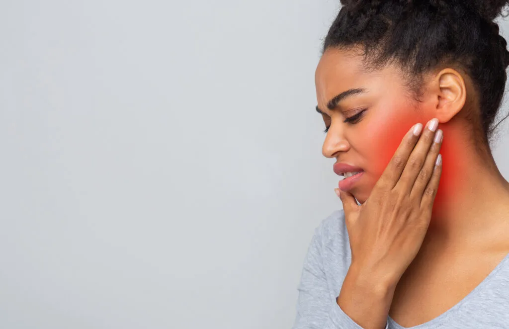 Image d’une femme tenant sa joue enflammée, souffrant de douleurs à la mâchoire causées par une dent de sagesse incluse, illustrant les symptômes courants du problème.