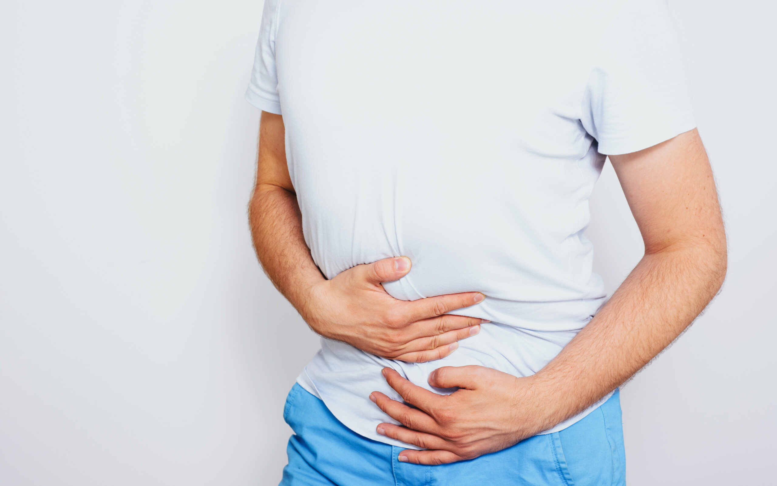 Douleurs abdominales : Causes, Types et Traitements Image d’un homme en t-shirt blanc et short bleu se tenant le ventre avec les deux mains, illustrant une douleur abdominale intense