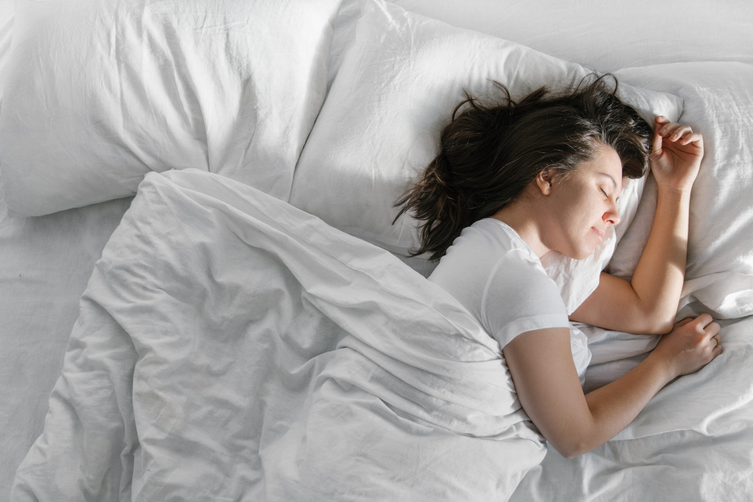 Sommeil : Pourquoi c’est important, les phases, REM et NREM Femme dormant paisiblement dans un lit avec des draps blancs, illustrant l’importance d’un sommeil de qualité pour la santé et le bien-être.